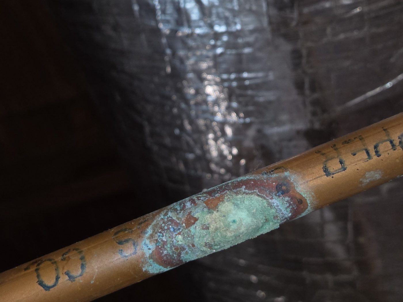 Close-up of green and rust-colored pitting corrosion on the underside of a copper water pipe at a pinhole leak
