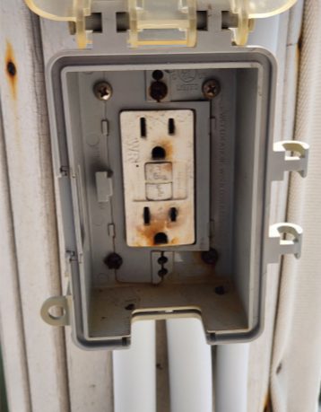 Exterior GFCI outlet on a Naples boat dock with rust staining and scorch marks inside the weatherproof box