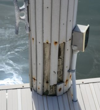 Cracked and deteriorated wood piling wrap boards with corroded fasteners on a Naples boat dock