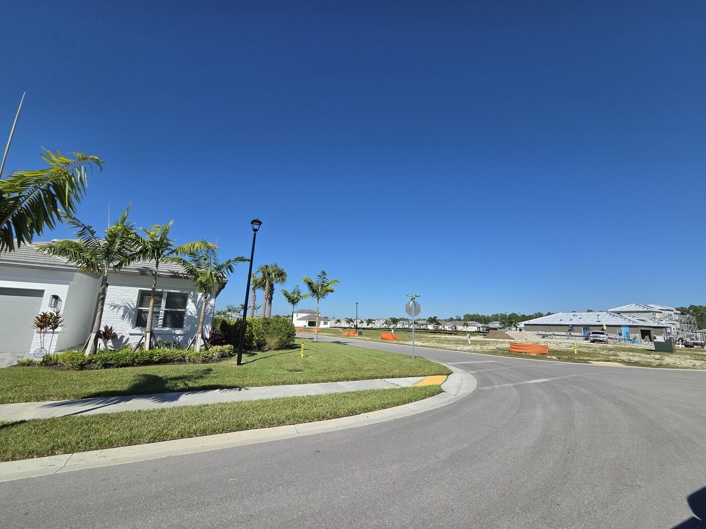 Completed home with palms and sod on a corner lot in Valencia Sky, Naples, with homes under construction in the background